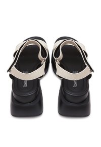 Paire de sandales à plateforme noires avec larges sangles beiges et fermetures réglables à scratch vues de dos.