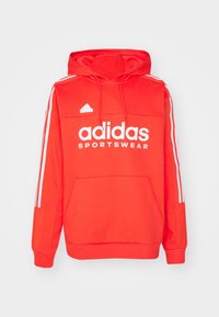 Felpa rossa Adidas con tasca a forma di canguro sul davanti, logo bianco e tre strisce bianche su ciascun maniche. Realizzata in tessuto morbido. Caratterizzata da un cappuccio con cordino.