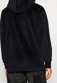 Svart huvtröja med en mjuk textur, försedd med dragsko i huvan och ribbade muddar. Designen är enkel, utan synliga logotyper eller mönster.