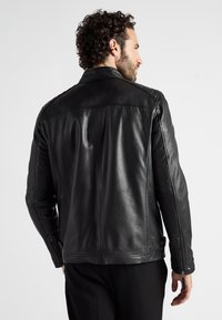 Svart läderjacka med en strukturerad design, iögonfallande krage, dragkedjeärmar och synliga sömnadsdetaljer. Slät textur.