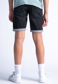 Shorts de mezclilla negra con dobladillos grises enrollados, con un ajuste relajado y dos bolsillos traseros. Llevados con zapatillas blancas y calcetines.