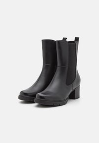 Par de botas de cuero negras hasta la mitad de la pantorrilla con paneles laterales elásticos, lengüetas, puntas redondeadas, tacones cuadrado y suelas de taco sobre un fondo blanco.