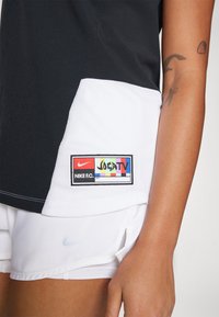 Czarny i biały sportowy top o teksturze dzianiny. Posiada wielokolorową łatkę z logo Nike oznaczoną "Joga TV" z boku.