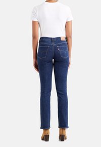 Dunkelblaue Jeans aus Denim mit Slim Fit, hinteren Taschen mit geschwungener Naht und einem Leder-Logo-Patch am Bund. Kombiniert mit braunen High-Heels.