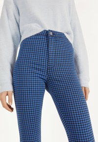 Blue and black checkered high-waisted pants with a front button closure and pocket details, paired with a light blue fuzzy sweater.
