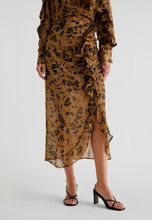 Braun gemustertes Kleid mit transparenter Textur, das Raffung und einen voluminösen Saum aufweist. Kombiniert mit schwarzen, schnürbaren High-Heels.