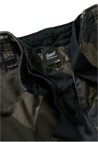 Kamouflagemönstrad tyg i nyanser av grönt och svart, med en etikett som läser "Brandit Individual Wear" och storlek "M". Har synlig sömnad.