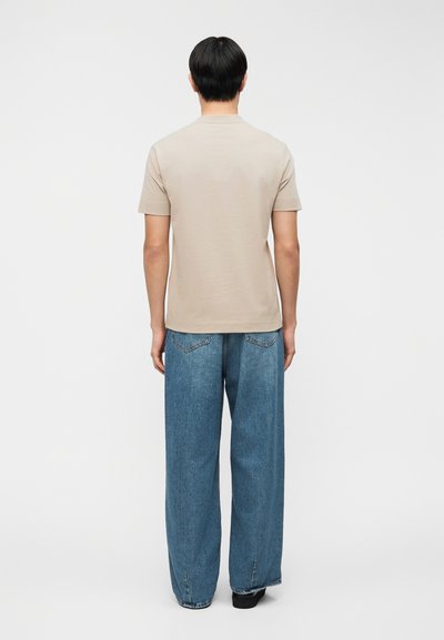 Μπεζ βαμβακερό t-shirt με κοντά μανίκια, συνδυασμένο με φαρδιά μπλε τζιν παντελόνια, με ίσια γραμμή και πίσω τσέπες.