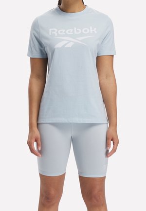 Personne portant un t-shirt Reebok bleu clair et un short ajusté assorti, debout devant un fond uni.