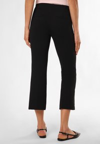 Zwarte cropped broeken van een getextureerde stof, met twee achterzakken en een getailleerde pasvorm. Gemaakt met zwarte platte sandalen.