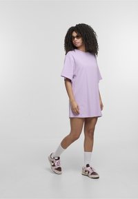Jasnofioletowa, oversize'owa sukienka t-shirt z krótkimi rękawami. Połączona z różowymi i brązowymi sneakersami oraz białymi skarpetkami do kostek dla swobodnego wyglądu.