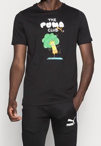 Camiseta negra con un gráfico divertido de un personaje de dibujos animados con un árbol, etiquetado como "EL CLUB DE PUMAS", fabricada en una suave mezcla de algodón.