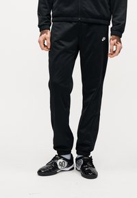 Μαύρο παντελόνι Nike για τρέξιμο με λεία υφή, ελαστική μέση και τσέπες με φερμουάρ. Συνδυασμένο με μαύρα και ασημένια αθλητικά παπούτσια.