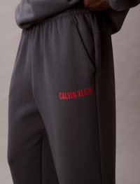 Szare spodnie dresowe z teksturowanej tkaniny, z czerwonym logo "CALVIN KLEIN", elastycznym pasem i bocznymi kieszeniami.