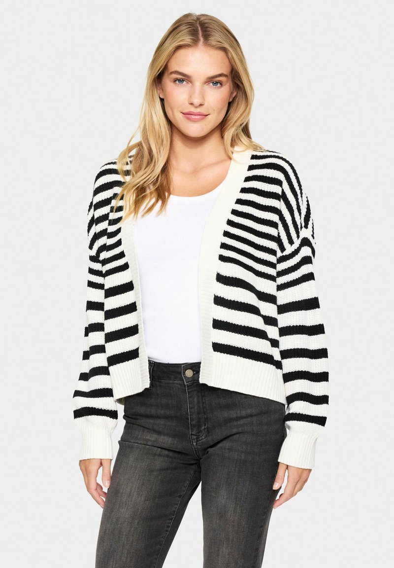 Cardigan à rayures noires et blanches, design court avec des poignets et un ourlet côtelés. Texture lisse, style à devant ouvert, associé à un haut blanc.