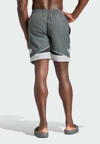 Gray swimming shorts with a white hem, black accents, and an elastic waistband. Features a side pocket and a distinct logo.