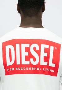 Λευκό βαμβακερό μπλουζάκι με μεγάλο κόκκινο ορθογώνιο γραφικό στην πλάτη, που απεικονίζει τη λέξη "DIESEL" και "FOR SUCCESSFUL LIVING" με έντονη λευκή γραφή.