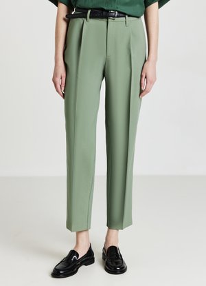 Grüne maßgeschneiderte Hose mit glatter Textur, gefaltetem Vorderteil, hoher Taille und knöchellang. Kombiniert mit schwarzen Slippers und einem passenden Gürtel.