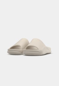 Beige slip-on sandals made of smooth material. Features an open-toe design with a contoured sole and no visible logos.