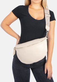 Hellbeige Leder Bauchtasche mit strukturierter Oberfläche, ausgestattet mit einem silbernen Reißverschluss und einem gemusterten, verstellbaren Tragegurt in neutralen Farbtönen.