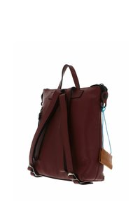 Sac à dos en cuir bordeaux avec une finition texturée, des bretelles réglables, une poignée supérieure et une petite étiquette marron attachée par un cordon bleu.