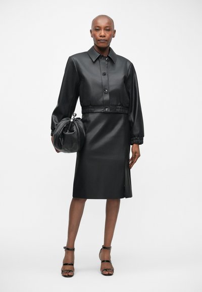 Crna kožna haljina s prilagođenim strukom, zatvaranjem na dugmad i dugim rukavima. Uparena s odgovarajućom crnom okruglom torbom i sandalama na remen.