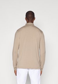 Ilgām piedurknēm beidzēts polo krekls ar apkakli, izgatavots no gludas auduma, ar delikātām šuvēm, valkāts ar baltām biksēm.