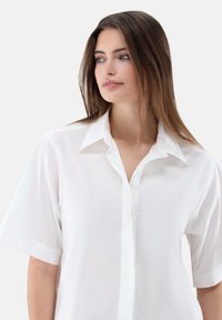 Weißes Kurzarmhemd mit Knopfleiste, klassischem Kragen und glattem, leichtem Stoff. Minimalistisches Design, ohne Muster oder Verzierungen.