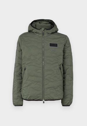 Quilted hooded jacket in olive green with a zip closure, side pockets, and a black fabric patch on the chest. Textured surface detail.