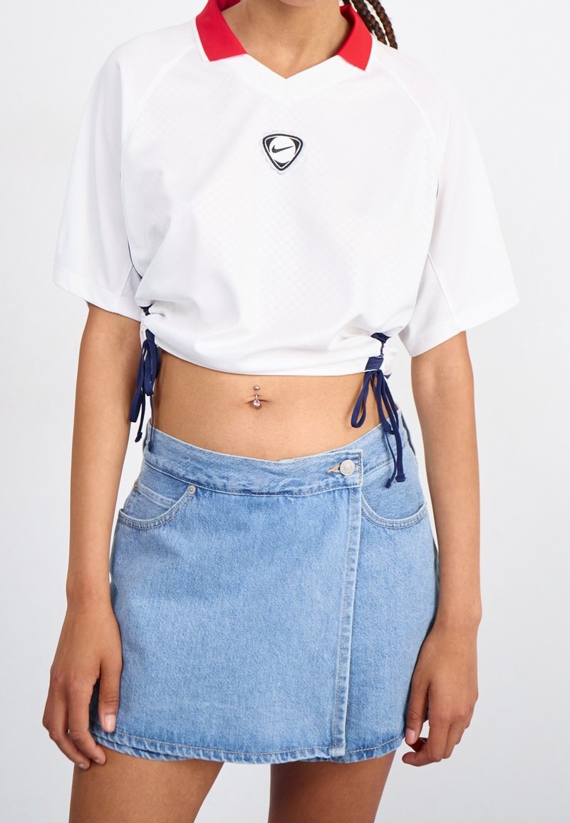 Chemise blanche à manches courtes avec un col rouge et des lacets bleus sur les côtés, assortie d'une mini-jupe en denim bleu clair avec une fermeture à boutons sur le devant.