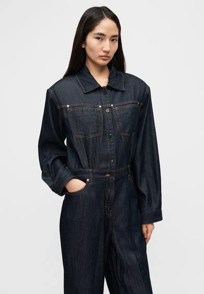 Σκούρο τζιν ολόσωμο φόρεμα με κουμπωτό μπροστινό μέρος, φαρδύ γιακά, δύο τσέπες στο στήθος και ελαστική μέση. Μακριά μανίκια με κουμπωτά μανσέτα, υφασμάτινη υφή.