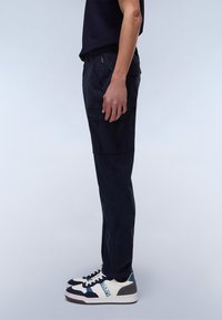 Navy cargo pants made of lightweight fabric. Features side pockets, a straight leg design, and reinforced stitching. Paired with multicolored sneakers.
