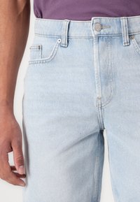 Svijetloplave traperice ravnog kroja, s prednjim džepom, zatvaranjem na gumbe i suptilnim detaljima šivanja. Glatka tekstura.