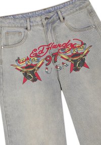 Jean en denim bleu clair avec texte coloré "Ed Hardy 1971" et deux graphiques de têtes de taureau avec de longues cornes et des arrière-plans en forme d'étoile rouge.