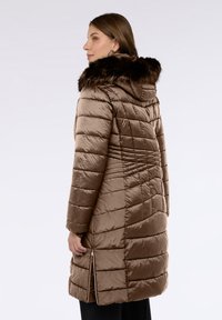 Abrigo acolchado marrón con capucha de piel sintética, cremalleras laterales y diseño acolchado. Textura suave con costuras estructuradas para brindar calidez y estilo.