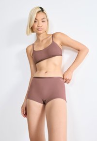 Brun sömlös bralette och matchande shortset, tillverkat av slät tyg med en minimal design och kontrasterande kant vid kanterna.
