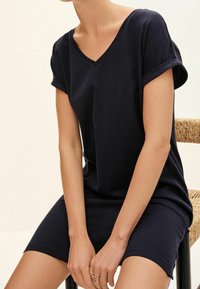 Tmavě modré šaty s krátkým rukávem, véčkovým výstřihem a ohrnutými rukávy, vyrobené z měkké tkaniny. Design má volný střih, dosahující do poloviny stehna.