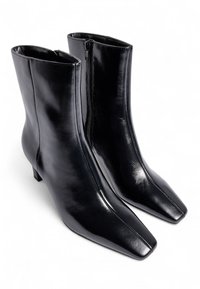 Botas de cuero negro hasta el tobillo con un acabado brillante, puntas cuadradas y un tacón bajo. Cuenta con una cremallera lateral para un fácil uso.