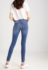 Högmidjade blå denim skinningjeans med en blekt finish, bakfickor och en smal passform, i kombination med vita sneakers.