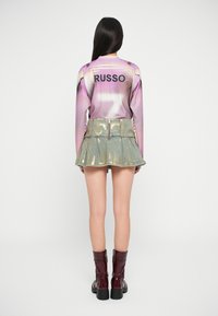 Top z dolgimi rokavi v roza barvi z napisom "RUSSO" in številko 7 v beli barvi, v kombinaciji s kratko, naborkano jeans krilo z zlatimi detajli in burgundskimi čezkolenskimi škornji.