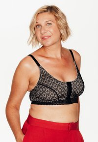 Reggiseno in pizzo nero con motivi geometrici, design in rete e chiusura frontale. Presenta spalline regolabili e un bordo a onda lungo il fondo.