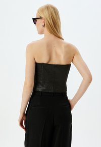 Sort strapless top med tekstureret stof, tætsiddende design og et rent silhuet. Bæres med højtaljede sorte bukser og accessoriseret med solbriller.