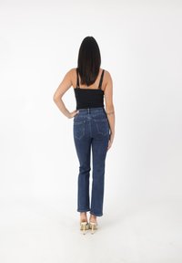 Czarny top na ramiączkach zestawiony z niebieskimi dżinsami o wysokim stanie. Dżinsy mają prosty krój i tylne kieszenie, z lekkim przetarciem.