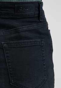 Svart denimjeans med en mjuk textur, med en enda bakficka och en läderetikett märkt "ONLY" på midjebandet.