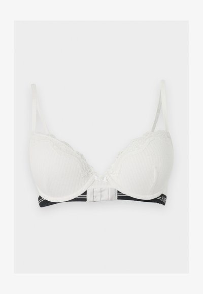 Hvid vadderet bh med blonderkant, justerbare stropper og sort elastisk underbånd med hvid tekstdetalje.