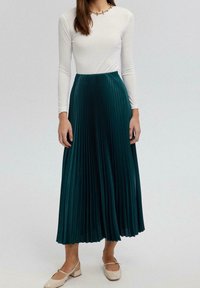 Teal geplooide maxi-rok gemaakt van zachte stof, gecombineerd met een aansluitende witte top met lange mouwen en lichtgekleurde platte schoenen. Simpele sieradenaccent.