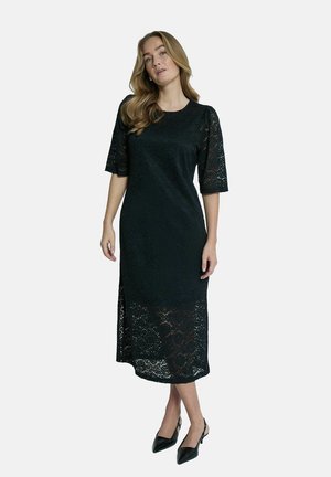 Black lace dress with short sleeves, knee-length hem, and side slit. Smooth texture with floral lace pattern. Paired with black pointed heels.