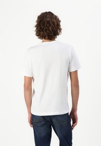 Hvid bomulds t-shirt med korte ærmer, der har en klassisk rund hals. Bagsiden er enkel uden grafik eller mønstre, suppleret med blå jeans.