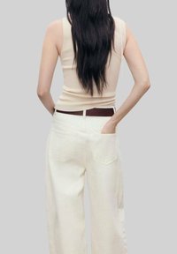 Beige tanktop med rund udskæring parret med højtsiddende, bredbenede, off-white bukser med sidelommer og baglommer.