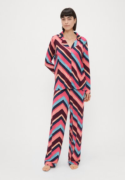 Kvinders pyjamasæt i pink, navy og blå med et zigzag-mønster; langærmet skjorte med knapper og løse bukser i blødt stof.
